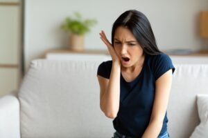 Woman in blue t-shirt holding her hand to her face in pain